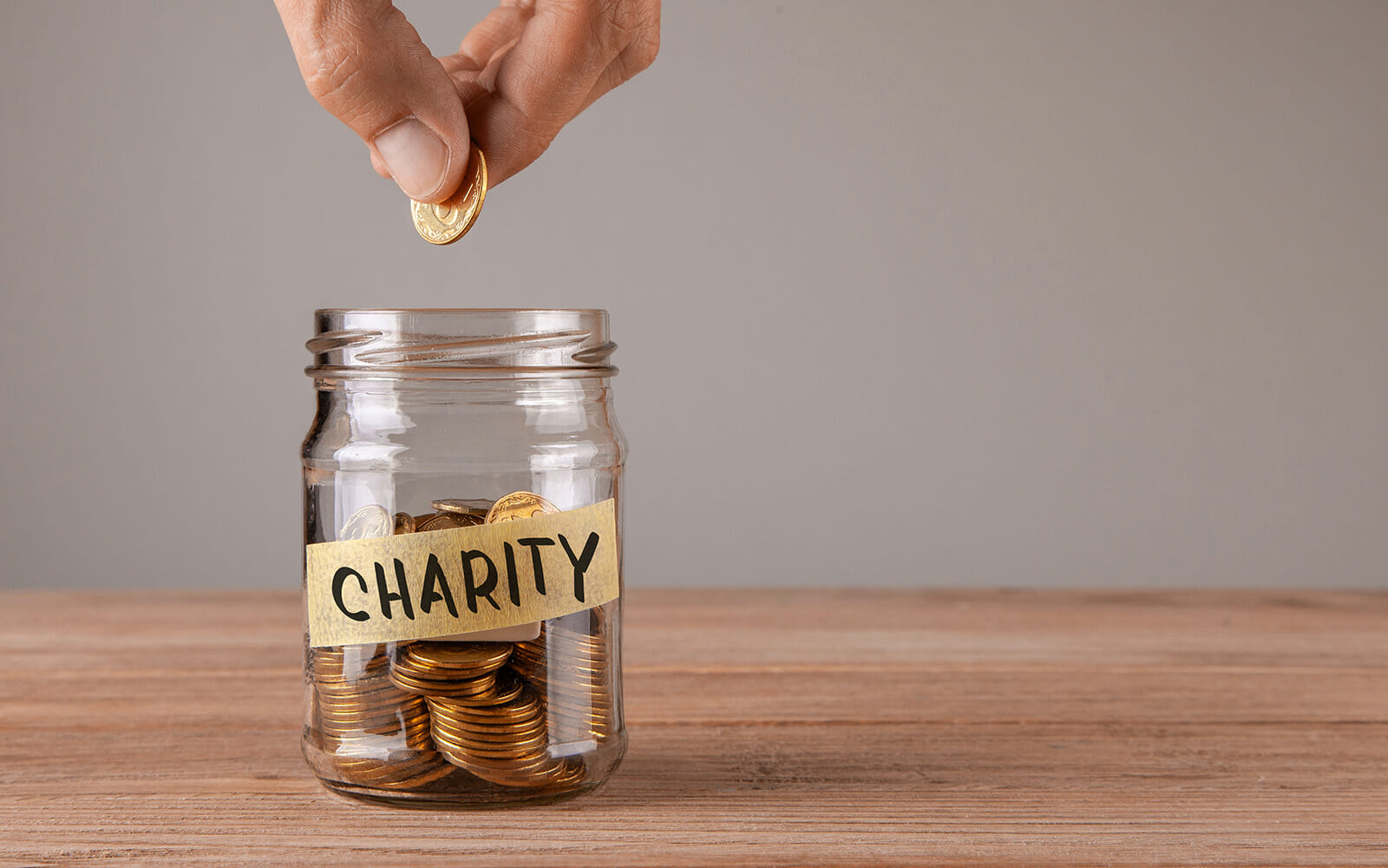 Hand putting coins into a jar marked charity